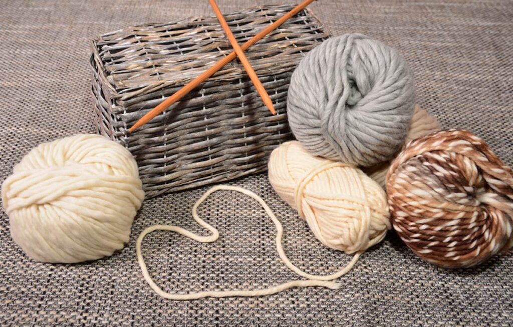 Four balls of yarn for crochet and knit patterns with a wooden hook and basket.